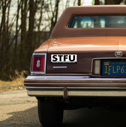 Vintage car with a 'STFU' sticker on the back, parked outdoors.
